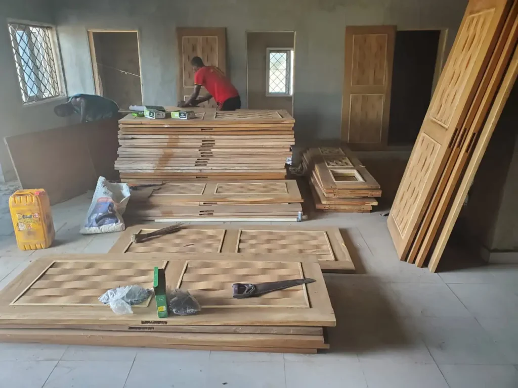 Nigerian craftsman working on a stack of finished wooden doors inside of the hospital